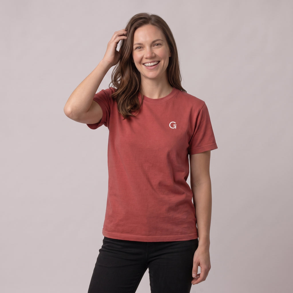A woman modelling a berry red t-shirt with a white embroidered ‘Clobber & Gear’ logo on the left chest, paired against a light grey studio background.