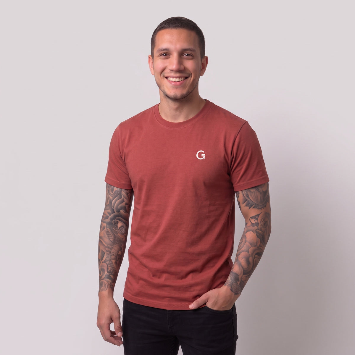 A man modelling a berry red t-shirt with a white embroidered ‘Clobber & Gear’ logo on the left chest, paired against a light grey studio background.
