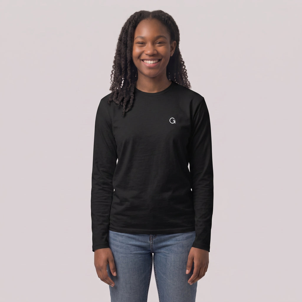 A woman modelling a black long sleeved t-shirt with a white embroidered ‘Clobber & Gear’ logo on the left chest, paired against a light grey studio background.