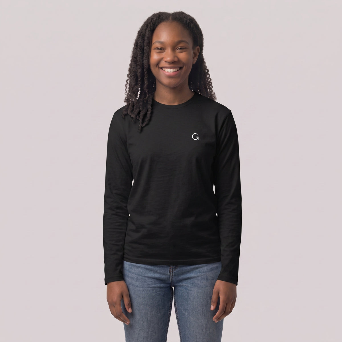 A woman modelling a black long sleeved t-shirt with a white embroidered ‘Clobber & Gear’ logo on the left chest, paired against a light grey studio background.