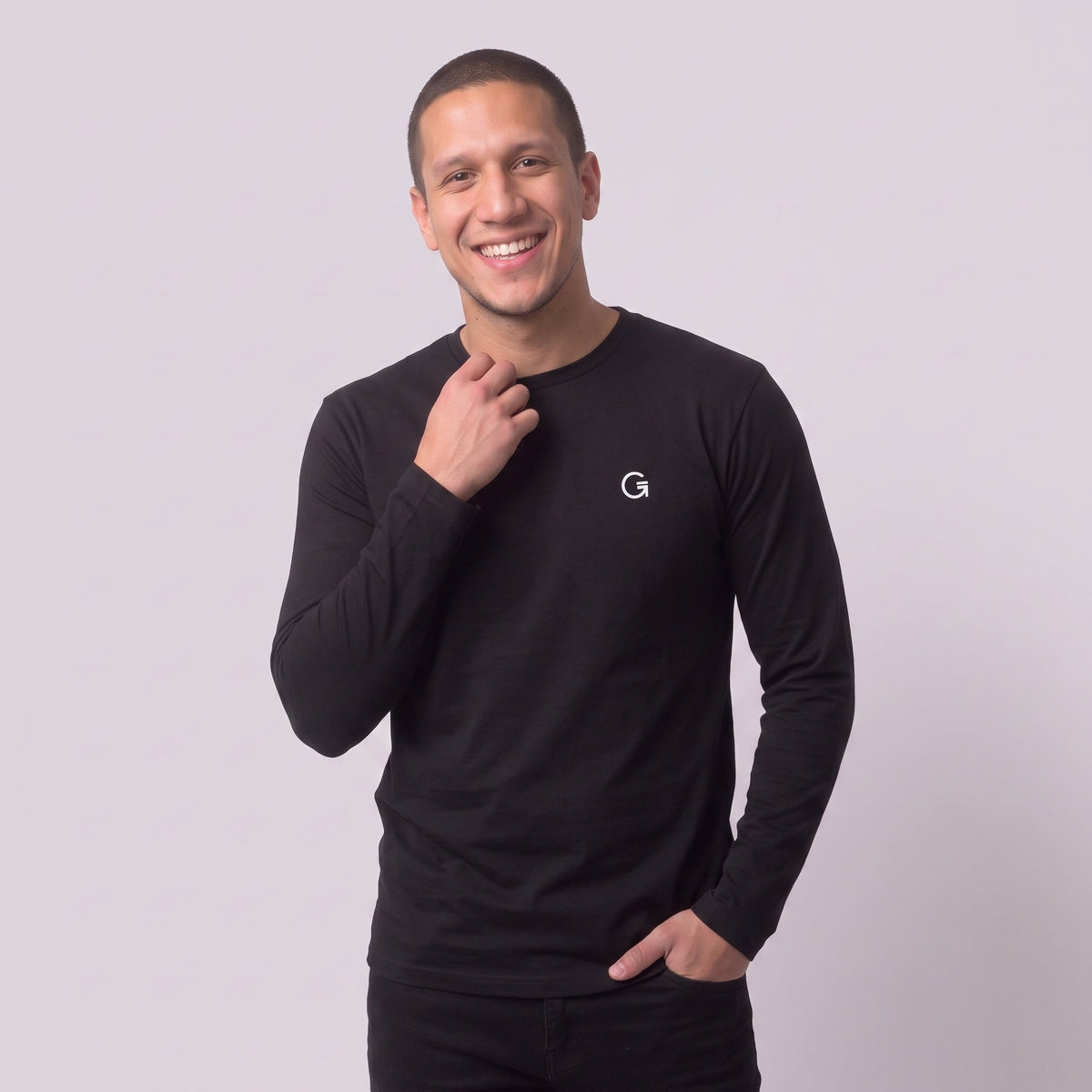 A man modelling a black long sleeved t-shirt with a white embroidered ‘Clobber & Gear’ logo on the left chest, paired against a light grey studio background.