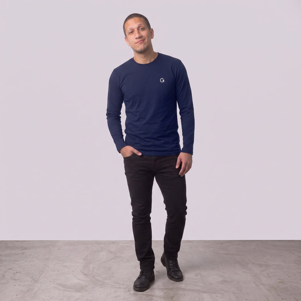 A man modelling a navy blue long sleeved t-shirt with a white embroidered ‘Clobber & Gear’ logo on the left chest, paired against a light grey studio background.