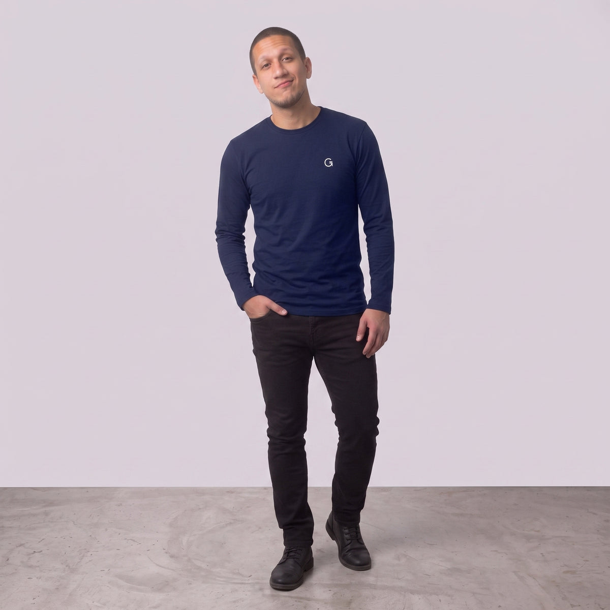 A man modelling a navy blue long sleeved t-shirt with a white embroidered ‘Clobber & Gear’ logo on the left chest, paired against a light grey studio background.