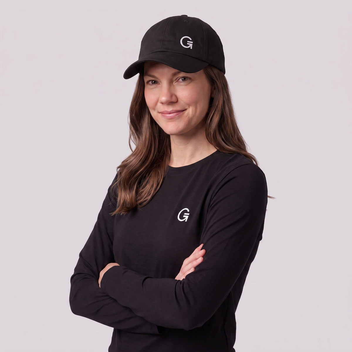 A woman wearing a black baseball cap with an offset white embroidered "Clobber and Gear" logo set against a light grey studio background.