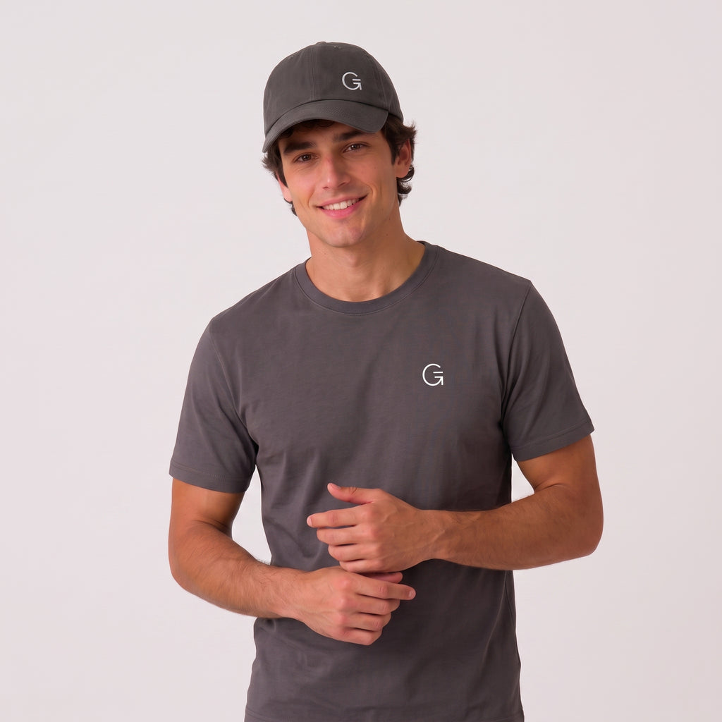 A man wearing a grey baseball cap with an offset white embroidered "Clobber and Gear" logo set against a light grey studio background.