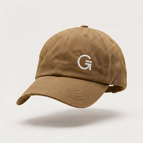 Front-three-quarter view of a tan dad cap featuring a white embroidered "Clobber & Gear" logo on the front left panel, set against a soft off-white background.