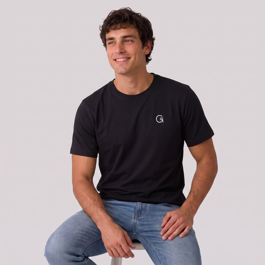 A man modelling a black tee with a white embroidered ‘Clobber & Gear’ logo on the left chest, paired against a light grey studio background.