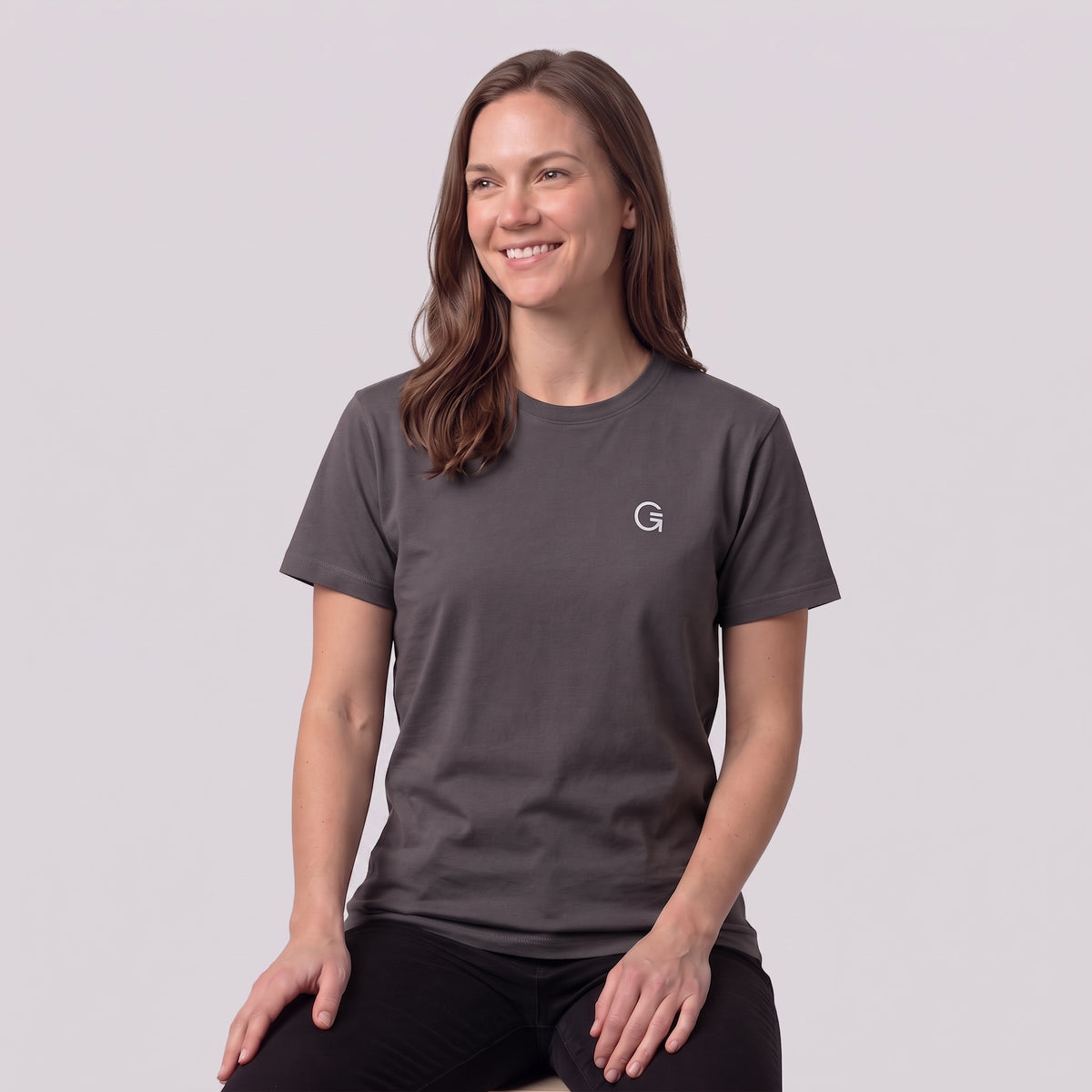 A woman modelling a charcoal tee with a white embroidered ‘Clobber & Gear’ logo on the left chest, paired against a light grey studio background.
