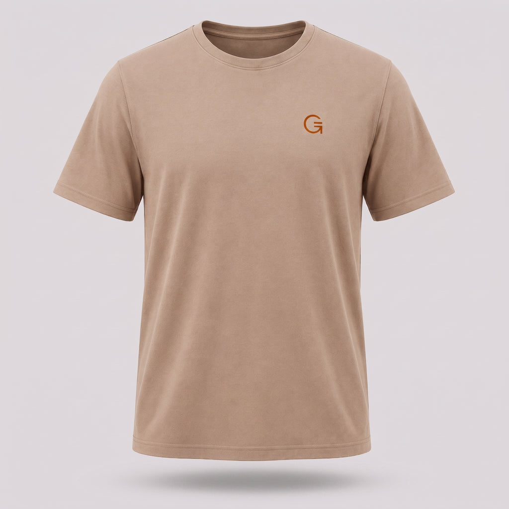 A ghost mannequin image of a latte-coloured crew-neck t-shirt with a burnt orange “Clobber & Gear” logo embroidered on the left chest, displayed on a neutral light grey background.